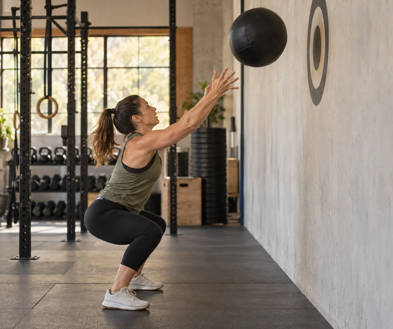 Mulher fazendo wall ball com bola medicinal na parede